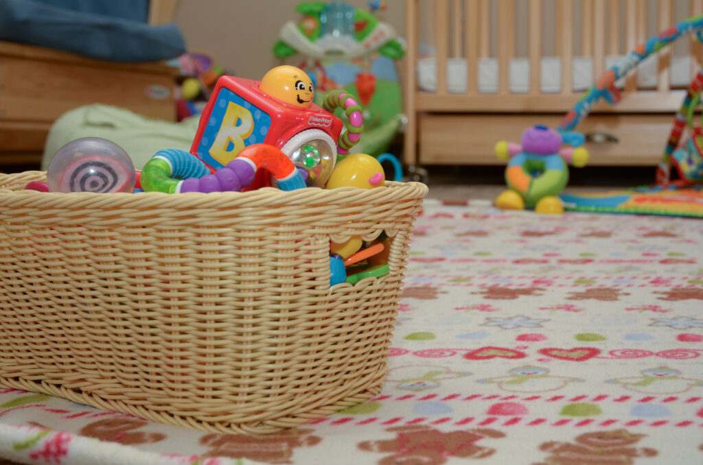 A basket on the floor is filled with baby toys, in a bright, colorful environment