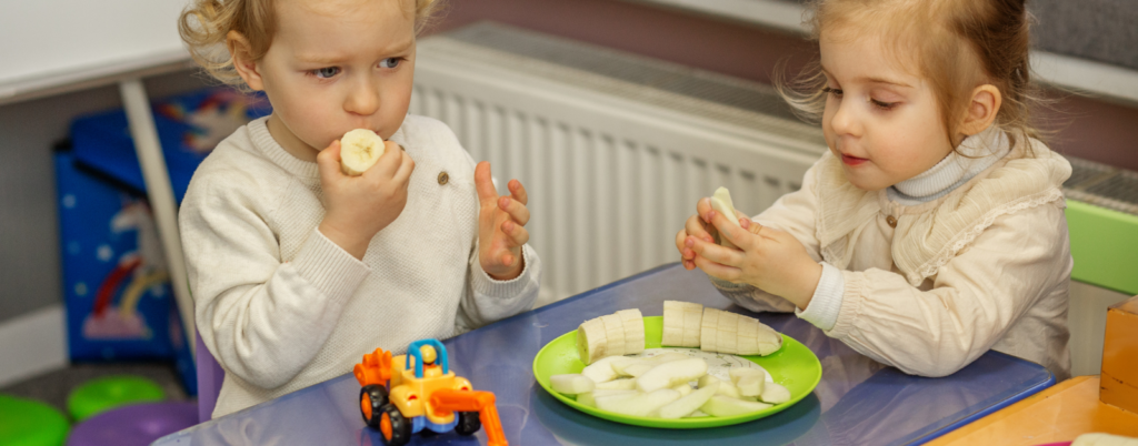 Two girls share a banana at snack time.