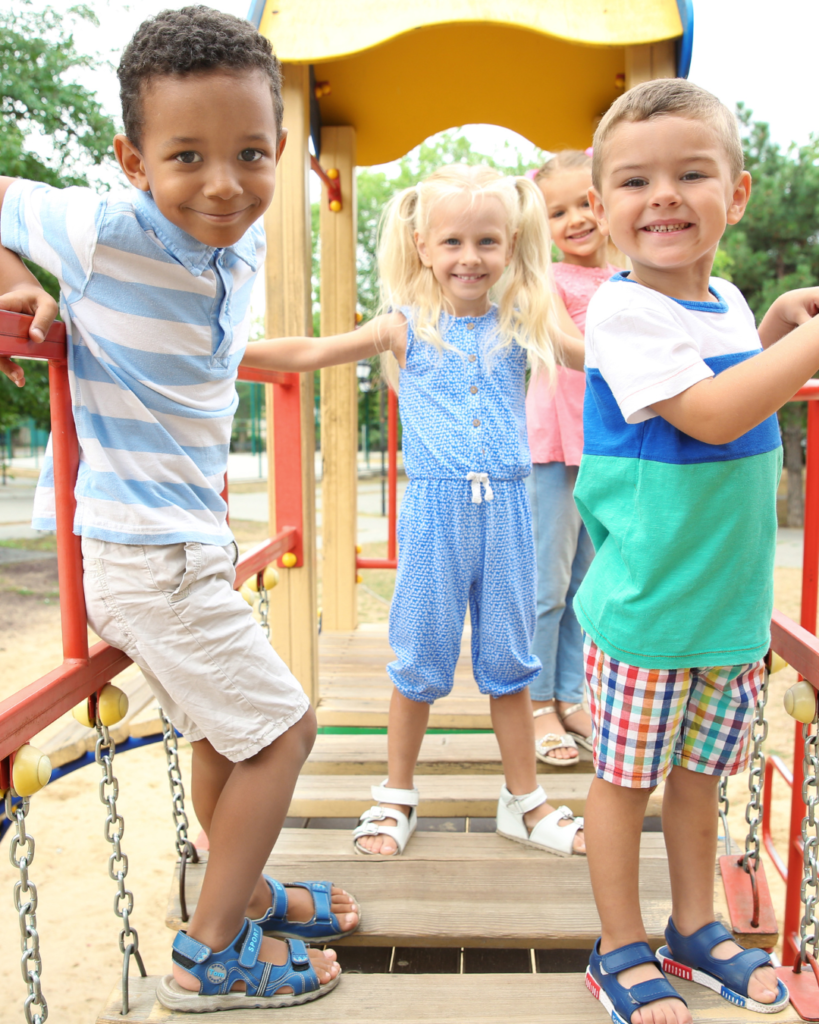 Three children stand on top of a playground structure, two boys and one girl.